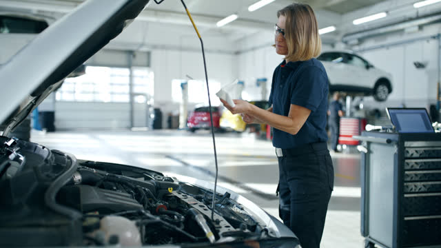 Female mechanic checking oil of car engine in auto repair shop