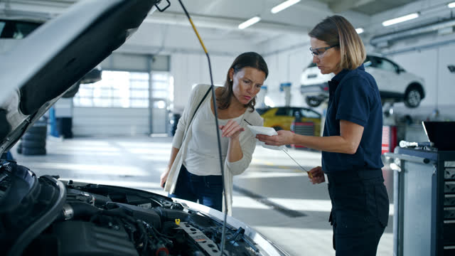 Female mechanic showing oil dipstick to customer in auto repair shop