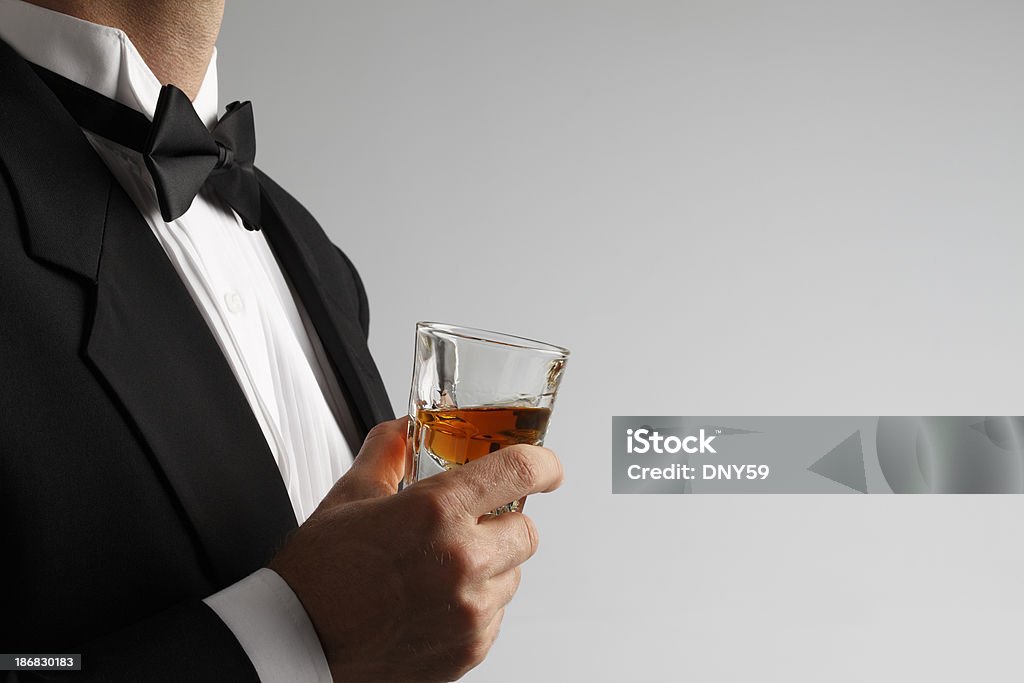 Człowiek w Smoking Trzymając Kieliszek whisky strzał na szarym tle - Zbiór zdjęć royalty-free (Alkohol - napój)