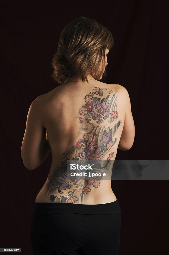 Beautiful tattoo on women's back "Flowing lotus flowers in japanese style on the back of thirty something women, black background." Back Stock Photo