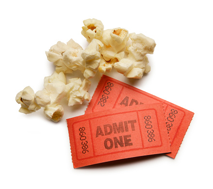 Three popcorn kernels and two red ticket stubs isolated on a white background. A soft shadow sits underneath the popcorn and ticket stubs