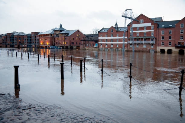 Flooded buildings "River in flood breaks its banks, covers the road and pavement, and floods the basements of the warehouses and apartments on the opposite bank. Focus on the foreground chain railings which mark the flooded pavement. This is the River Ouse in the centre of York, UK." ouse river photos stock pictures, royalty-free photos & images