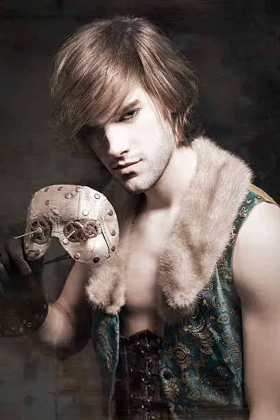 Male model posing in steampunk clothing holding a mask. Mysterious mood and a grungy look.