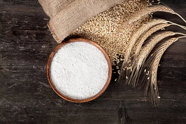 Flour and wheat grains with wheat ears on wooden background