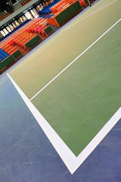Professional hard court surface tennis court. Dark background. Spectator seats in the background.