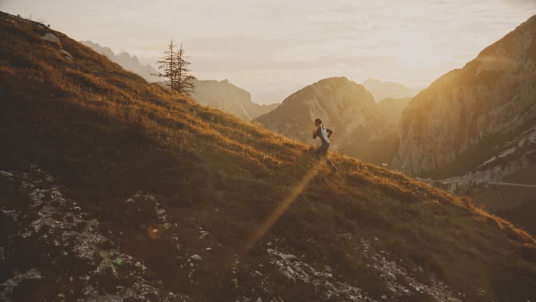 Woman Jogging up Grassy Hill in Sunny Mountains at Sunrise. Recreation in unspoilt nature.