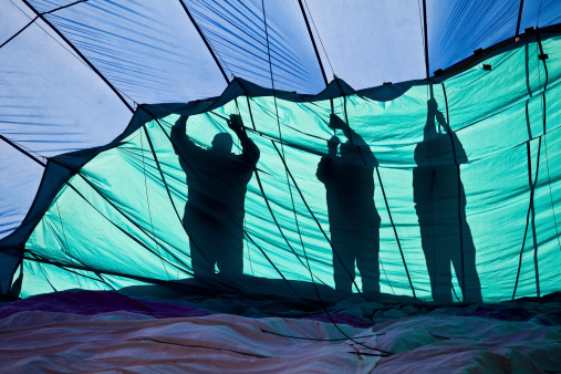 Silhouette of three people preparing a hot air balloon for launch.