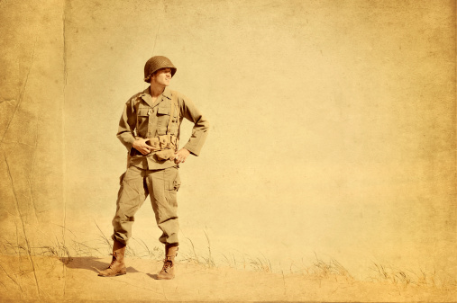 Faded picture of World War II American Infantryman standing on a lonely beach.  Gazing across to right of image as if to scan the horizon. 