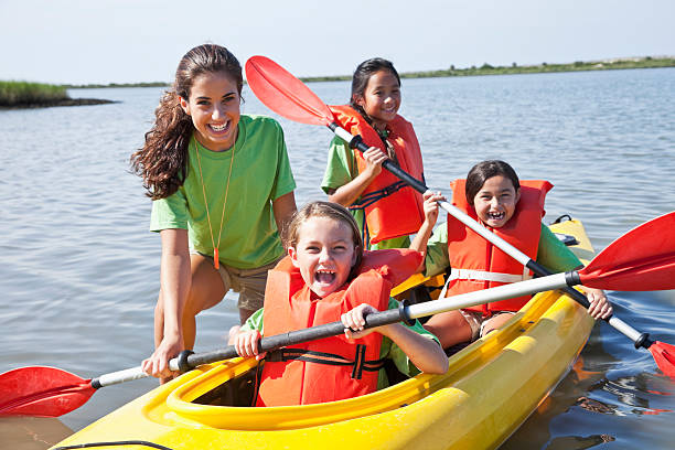 Girls in a double kayak Teenage girl (17 years) helping children in kayak (8-9 years).  Main focus on camp counselor and little girl in front. canoe photos stock pictures, royalty-free photos & images