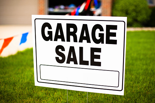 Garage sale sign on the front yard of a suburban house.