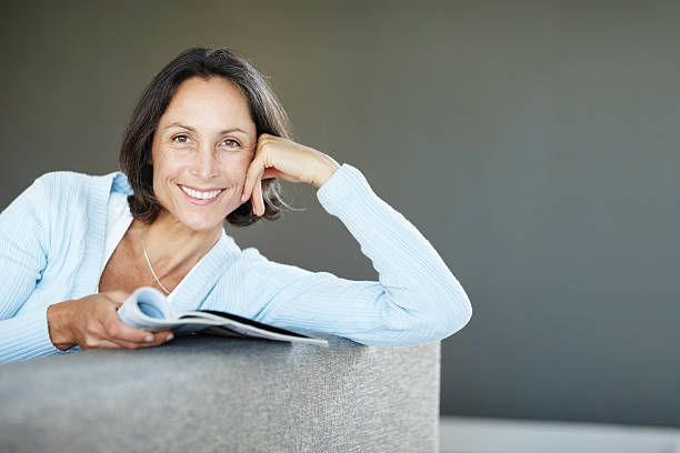 istock Pretty mature lady with a magazine relaxing on sofa 186836144
