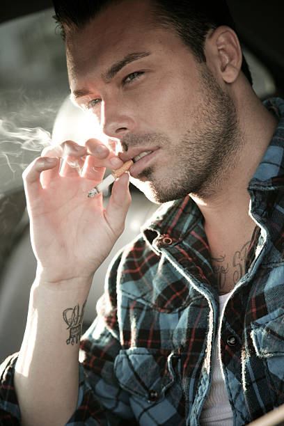 Adult Man sitting on a bench at public park smoke a cigarette