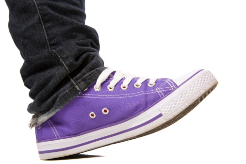 A purple canvas sport shoe stepping forward isolated on white with shadow.