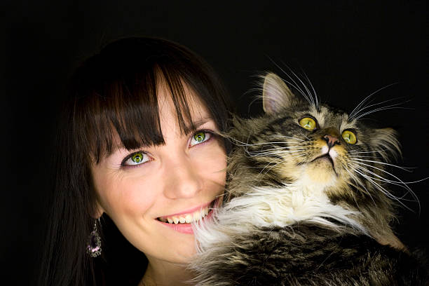 Portrait of a young woman holding her Maine Coon cat. Isolated on black.