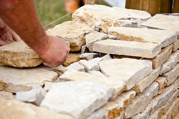 Drystone Wall Creation "A craftsman waller constructing a traditional drystone wall, with no mortar, from Cotswold stone, which is limestone. With an abundance of stone geographically available, dry stone walls to mark boundaries and enclose property have been constructed in the Cotswolds, England, since the Neolithic ages. The stones are carefully chosen for shape and size and laid so that rainwater will drain through the wall naturally." mason craftsperson stock pictures, royalty-free photos & images