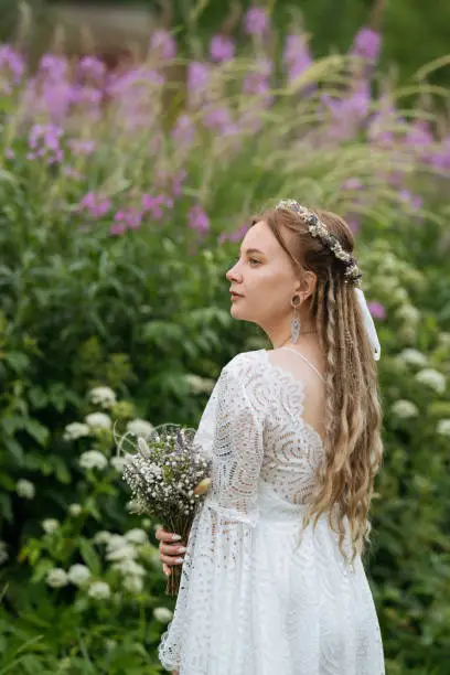 The free-spirited essence of a young adult bride in a flowing boho-style dress, standing gracefully amidst nature's beauty.