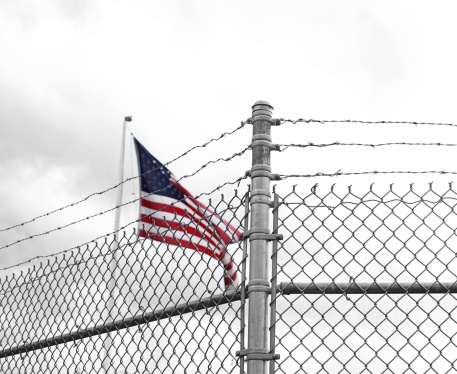 American Flag behind a Barbed Wire Fence with Selective Focus on Foreground.