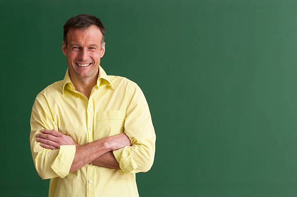 A smiling teacher with arms crossed in front of chalkboard happy teacher at blackboard - add your text rolled up sleeves stock pictures, royalty-free photos & images