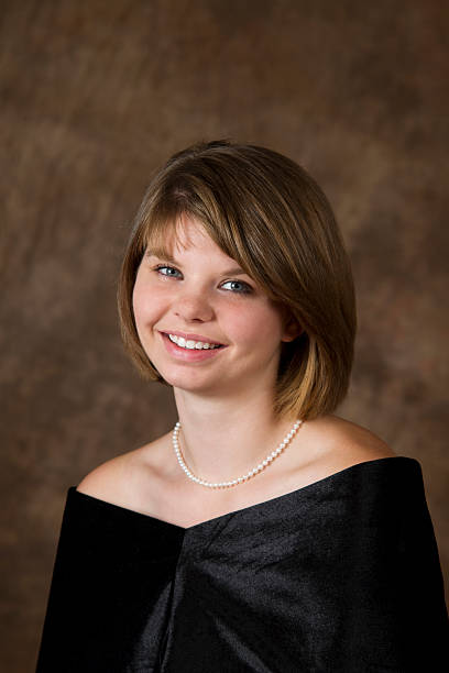 Young girl in black top posing for her portrait  Seen here is a 19 year old young lady sitting for her High School Senior portrait wearing a traditional simple black drape and pearls. Head cocked. high school photos stock pictures, royalty-free photos & images