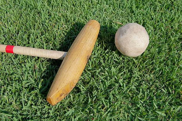 A polo mallet and ball sit on a green grass field.  Horizontal orientation.