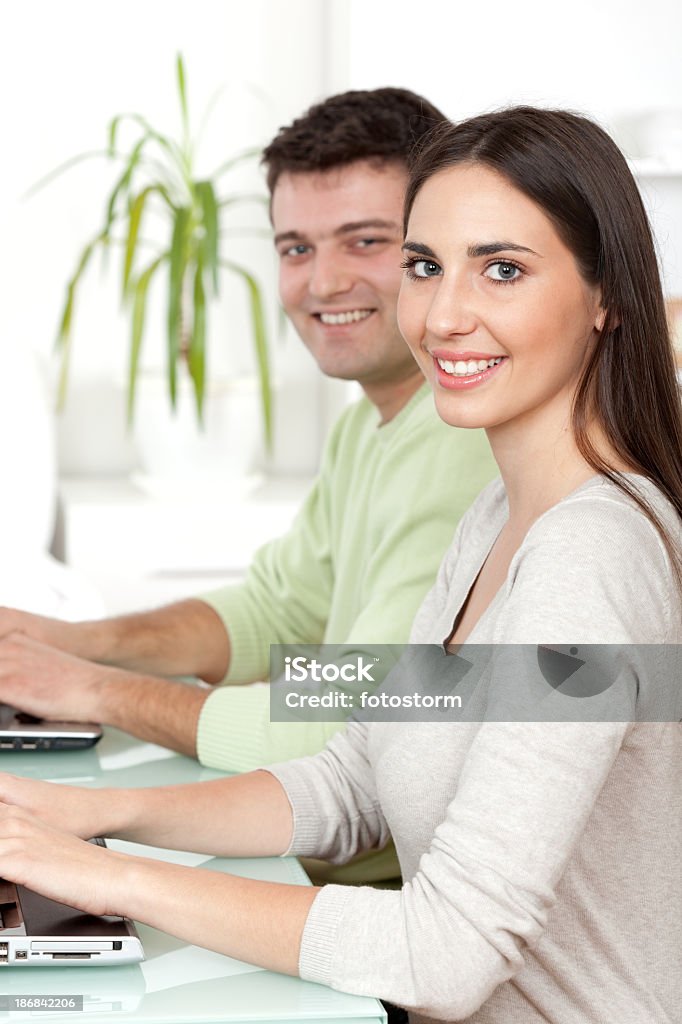 Two young students working on laptop computer Smiling young female and male student sitting by the table and using laptop computer indoors. Adult Stock Photo