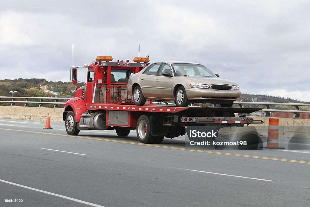 Tilt Bed Tow Truck Rear quarter view of a tilt bed tow truck on a highway carrying a nondescript vehicle. Tow Truck Stock Photo