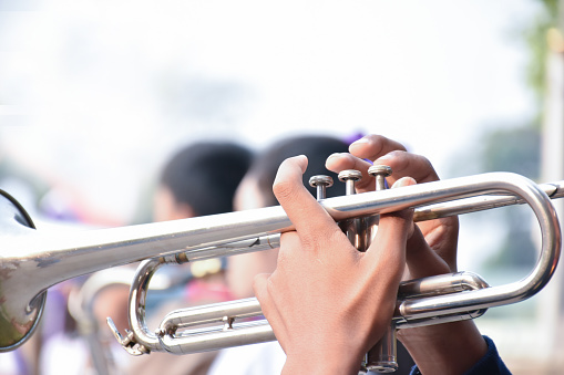 Trumpet instrument holding in hands of Asian student who playing it at a ceremony to honor the national flag in the morning. Soft and selective focus on trumpet.