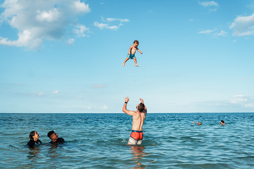 Young happy couple have fun at sea beach. Children run, jump high into water. Popular travel destination. Family summer vacation with kids at tropical island.