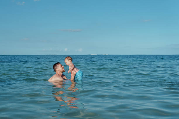 Loving father plays with toddler son in the ocean stock photo