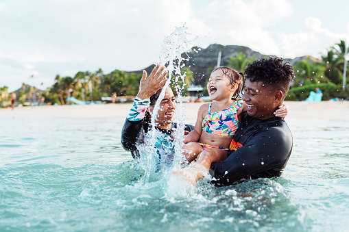 An adorable three year old Eurasian girl laughs while splashing in the ocean with her Hispanic aunty and Pacific Islander uncle.