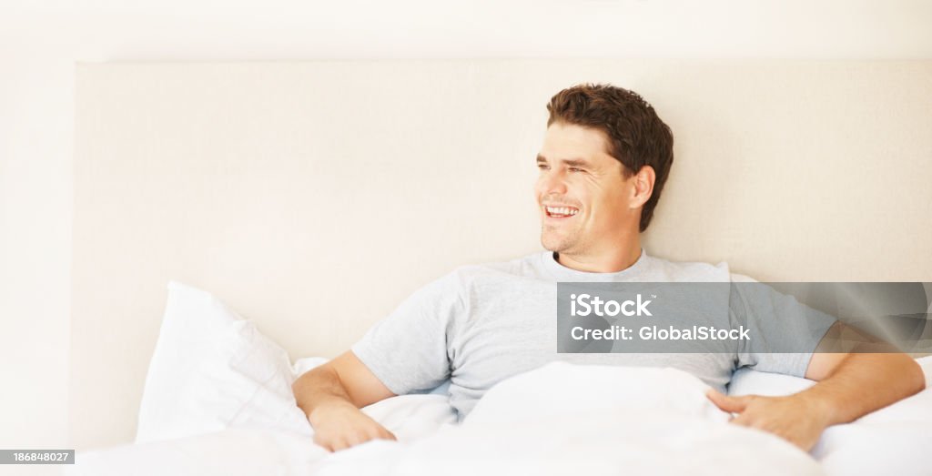 Smart mid adult man sitting in bed smiling Happy handsome mid adult man sitting up in bed 30-34 Years Stock Photo