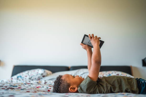 istock Lovely Mixed Race Boy Explores E-Books on Comfy Bed at Home 1868481519