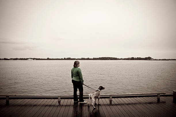 Woman pet owner walks her dog by Lake Ontario. Colors of been enhanced for creative and artistic effect. Visible grain.