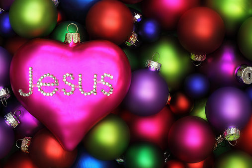 Heart shaped ornament with Jesus in rhinestones on top of multicolored Christmas ornaments to symbolize that Jesus is the Heart of Christmas.