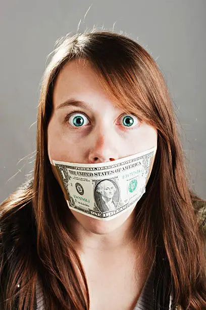 This young woman seems very shocked by being gagged with a US one dollar bill; she wants to have her say and freedom of speech is her right.
