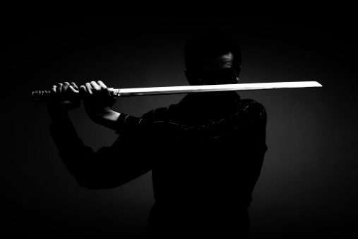 Contemporary ninja in the shadows posing with sword