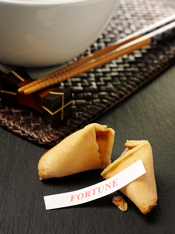 Broken Chinese fortune cookie with a fortune label on a slate background with chopsticks and a Chinese bowl. Click on the links below to see more food and business images.