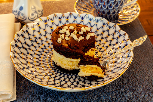 Layered dark and white chocolate dessert on a fancy bone China plate tipped with gold and a silver spoon.