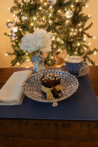 Hot chocolate and layered dark and white chocolate dessert on a fancy bone China plate tipped with gold and a silver spoon in front of a Christmas tree.