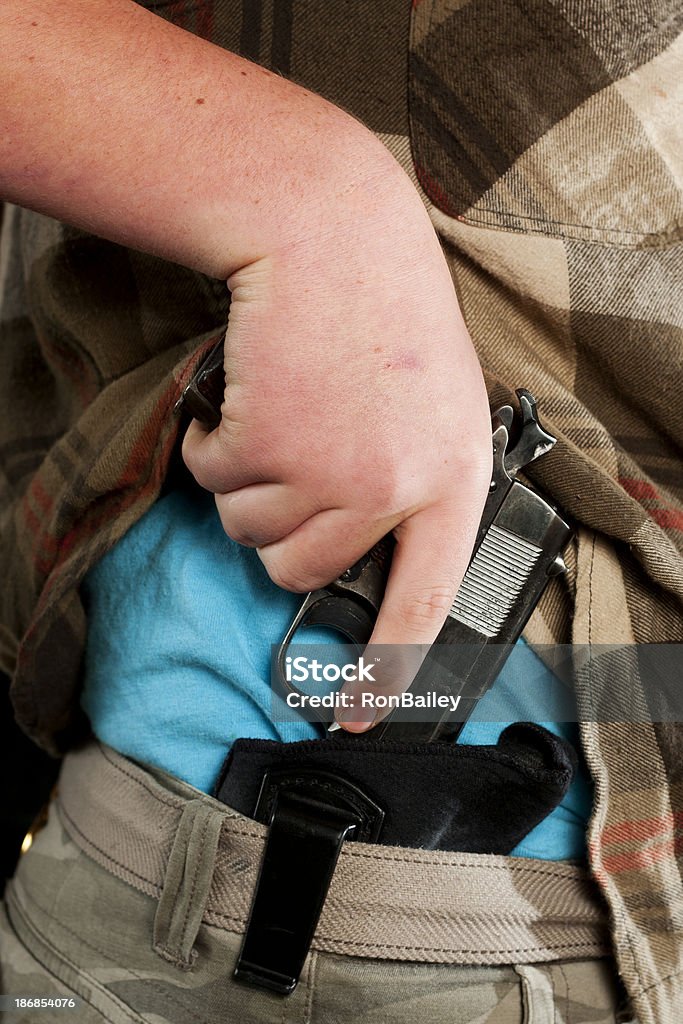 Concealed Carry Firearm Drawn From an Inside-the-Waistband Holster A caucasian man drawing a .45 caliber 1911 pistol from an IWB (inside the waistband) holster under his shirt.All images in this series... Hiding Stock Photo