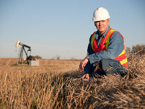 Oil Worker in Safety Gear at Well Pumpjack Oil worker engineer in safety gear inspects the soil near an oil well pumpjack.  Alberta Canada in the fall. geologist stock pictures, royalty-free photos & images
