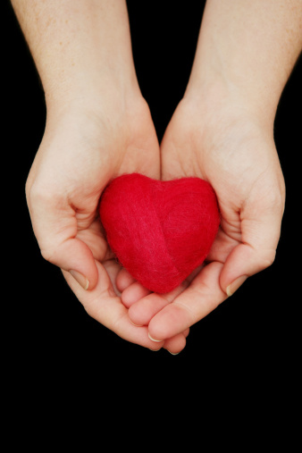 A woman's hands holding out a red felted heart (made by me).  Isolated on black.