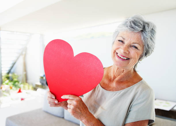 "Smiling, elderly woman holding red shaped heart"