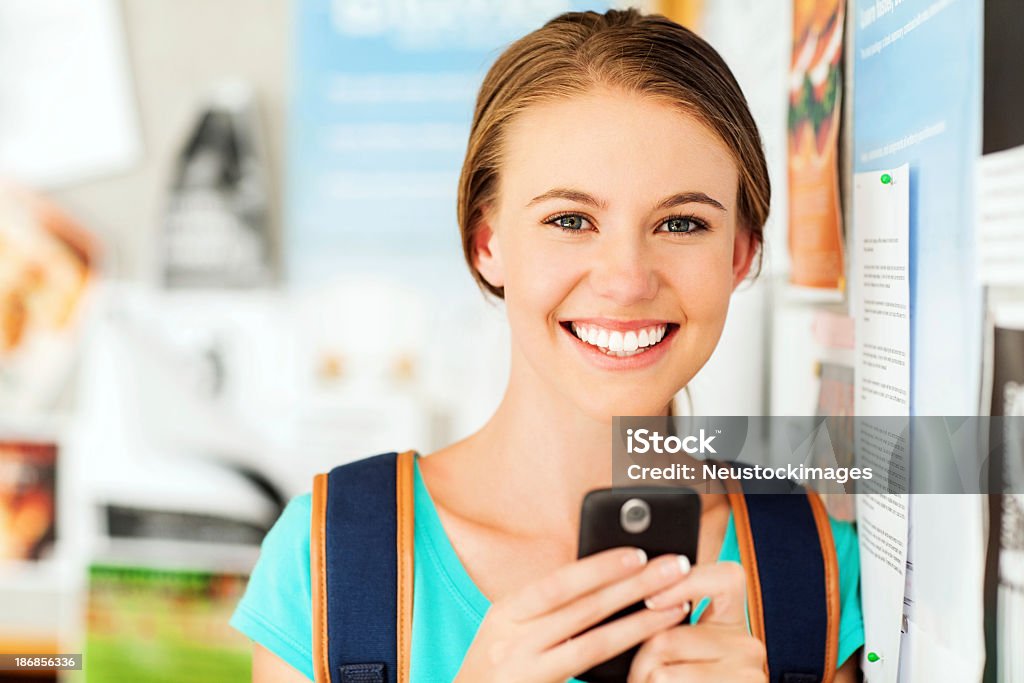 Chica mediante teléfono inteligente mientras que apoyarse en un panel de anuncios - Foto de stock de 16-17 años libre de derechos