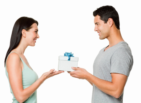 Attractive young couple smile at one another while holding a small gift box between them. Horizontal shot. Isolated on white.