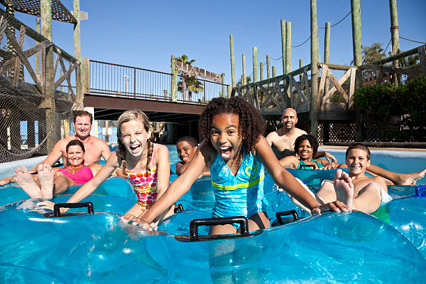 A group of men, women and children in inner tubes, floating down the lazy river at a water park.  The girls in the front are shouting with excitement.