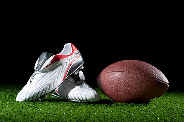 Gridiron ball and boots on grass Gridiron ball and boots on grass at night studded footwear stock pictures, royalty-free photos & images