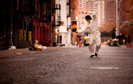 A kung fu martial artist training with his Shaolin Staff in a grungy alley way in New York City.