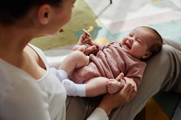 Laughing Baby Girl on Mothers Lap High angle view at cheerful newborn lying on knees of mom holding baby hands at home cute baby laughing stock pictures, royalty-free photos & images