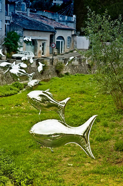 Shoal of silver fish balloons flying above the grassy banks of a river. Trompe l'oeil effect. Shows the saying 'If fish could fly'